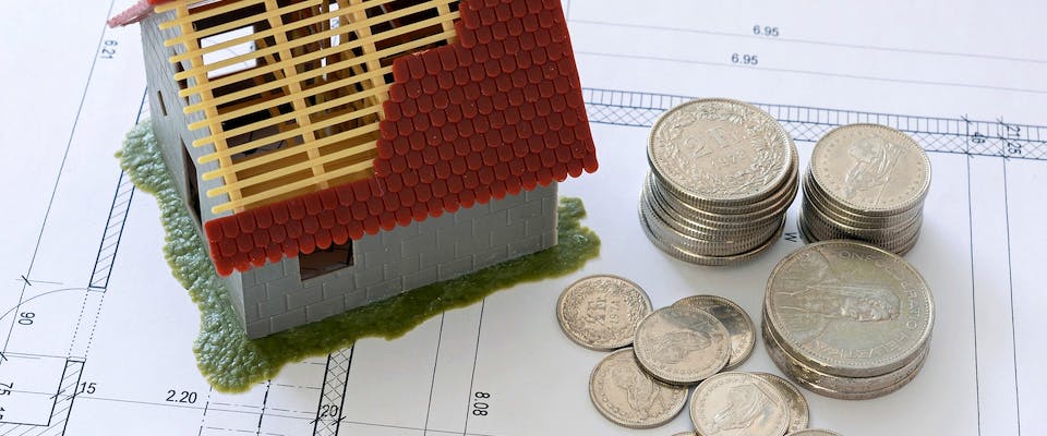 Hausmodell mit Münzen auf Bauplan